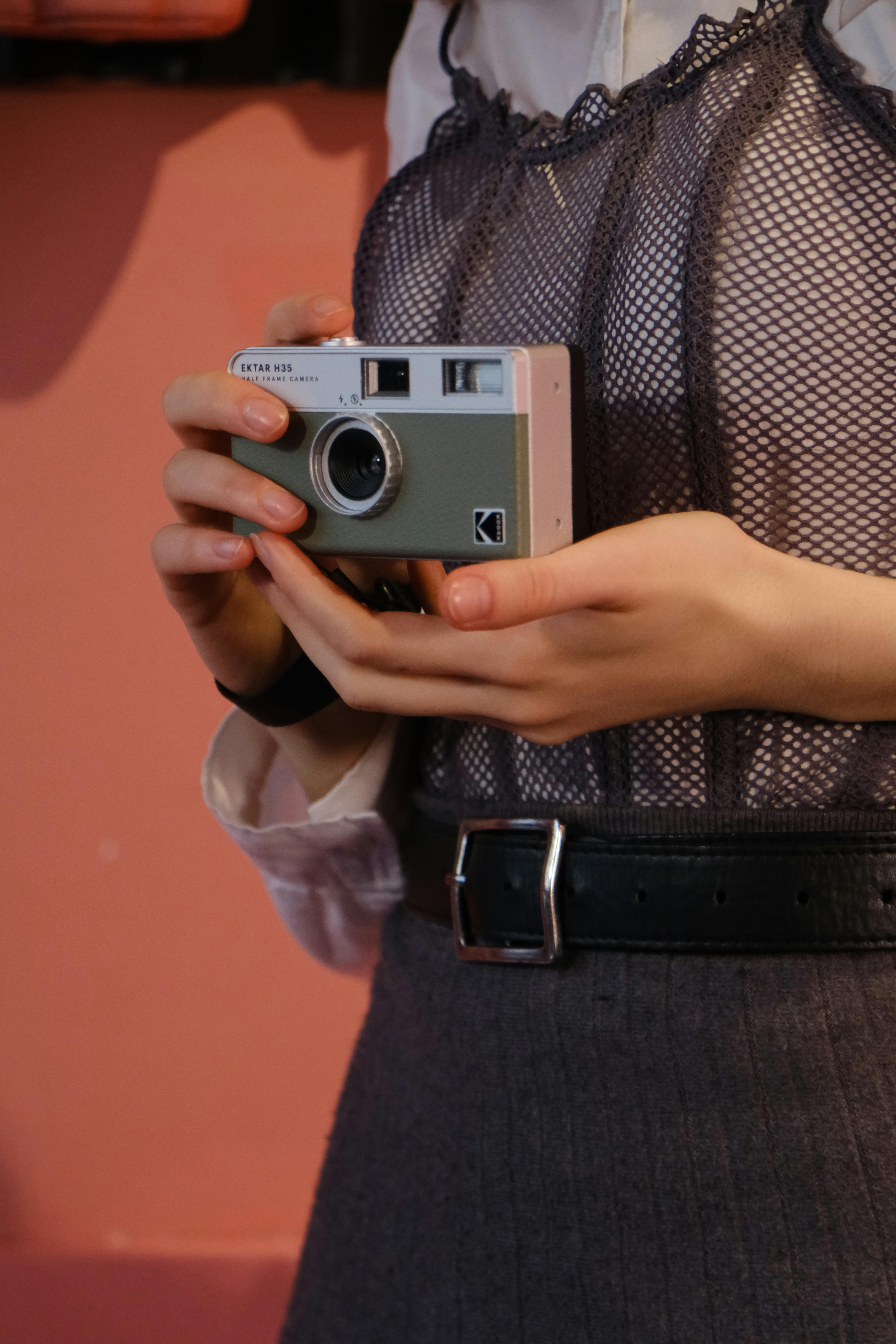 Close-up of a woman holding a stylish vintage camera against a warm background.