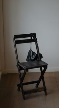 A sleek wooden chair holding a black leather bag in a minimalist room setting.