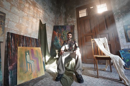 Artist sitting among abstract paintings in an atmospheric studio.
