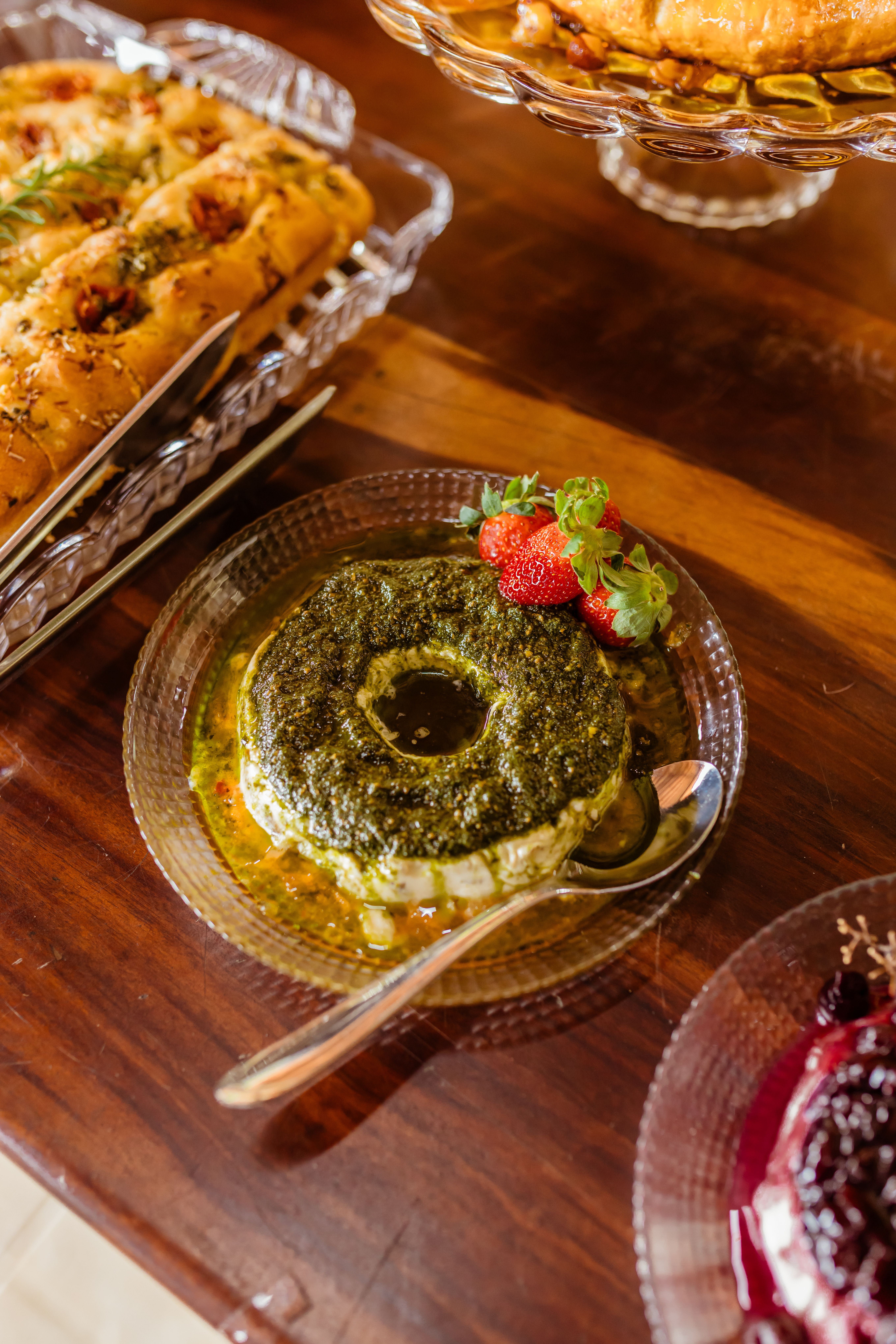 A mouth-watering pesto-covered cheese dish garnished with strawberries served on a glass saucer.