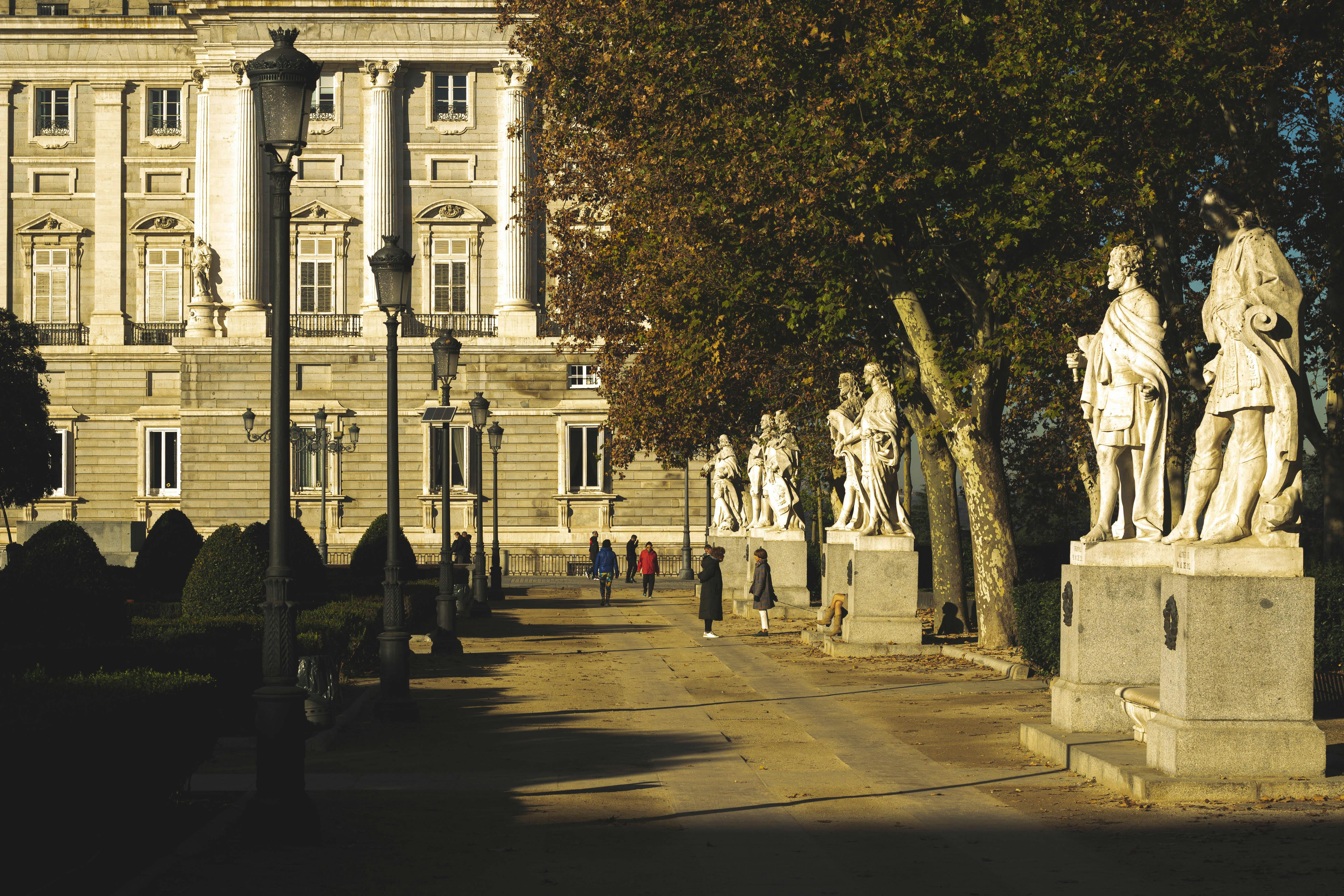 Statuary-lined walkway at the Royal Palace of Madrid, bathed in summer sunlight, showcasing classic European architecture.