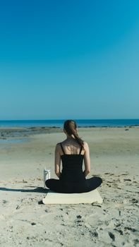 Woman in meditation pose on a serene beach, embracing peace and relaxation.