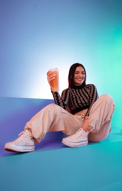 Smiling woman poses stylishly in studio, holding an orange drink.