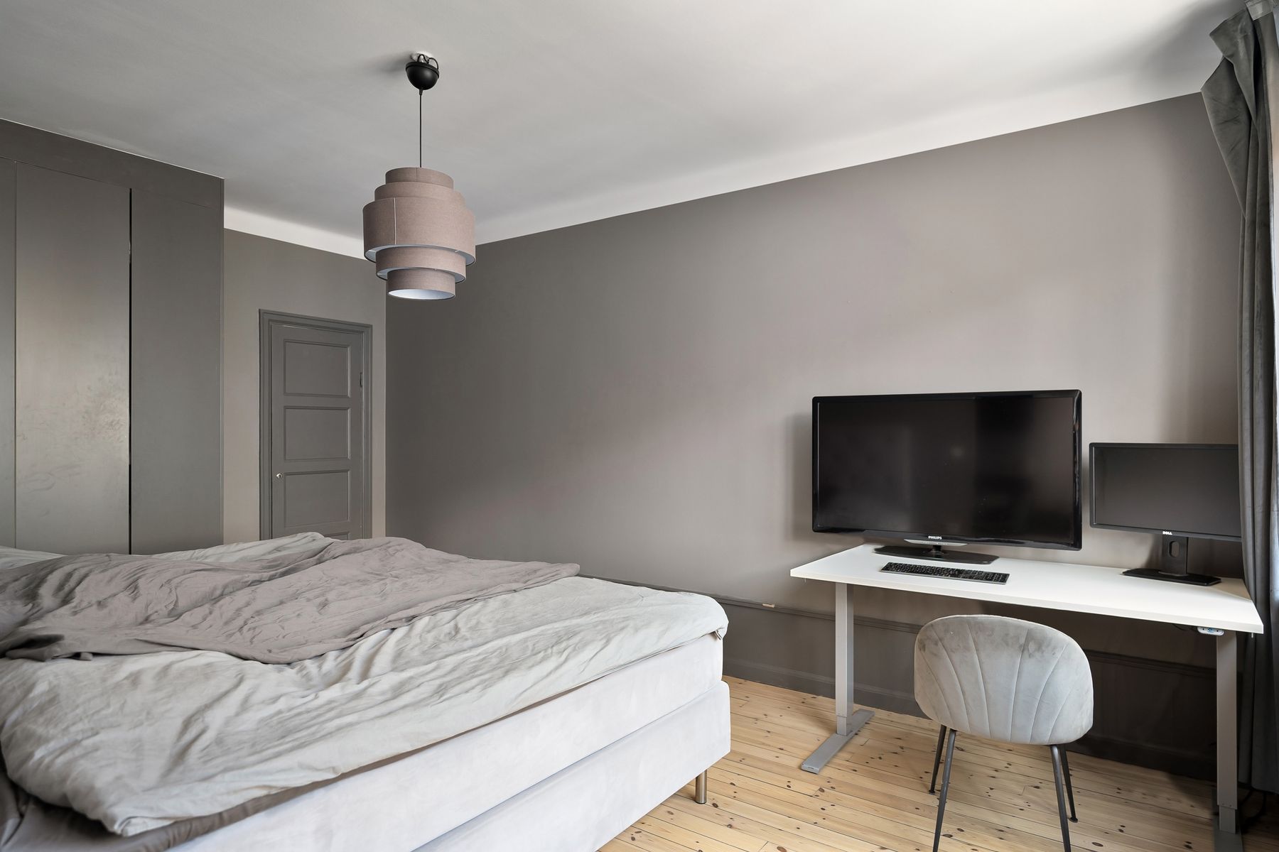 Desk with monitors beside a gray bed, television and open work storage