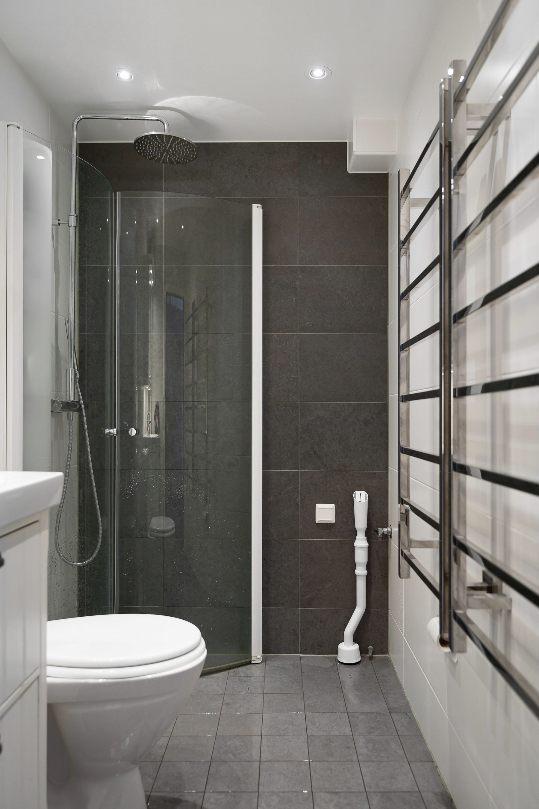Grey tiled bathroom with a clear glass shower enclosure, wall-mounted toilet and ladder towel radiator