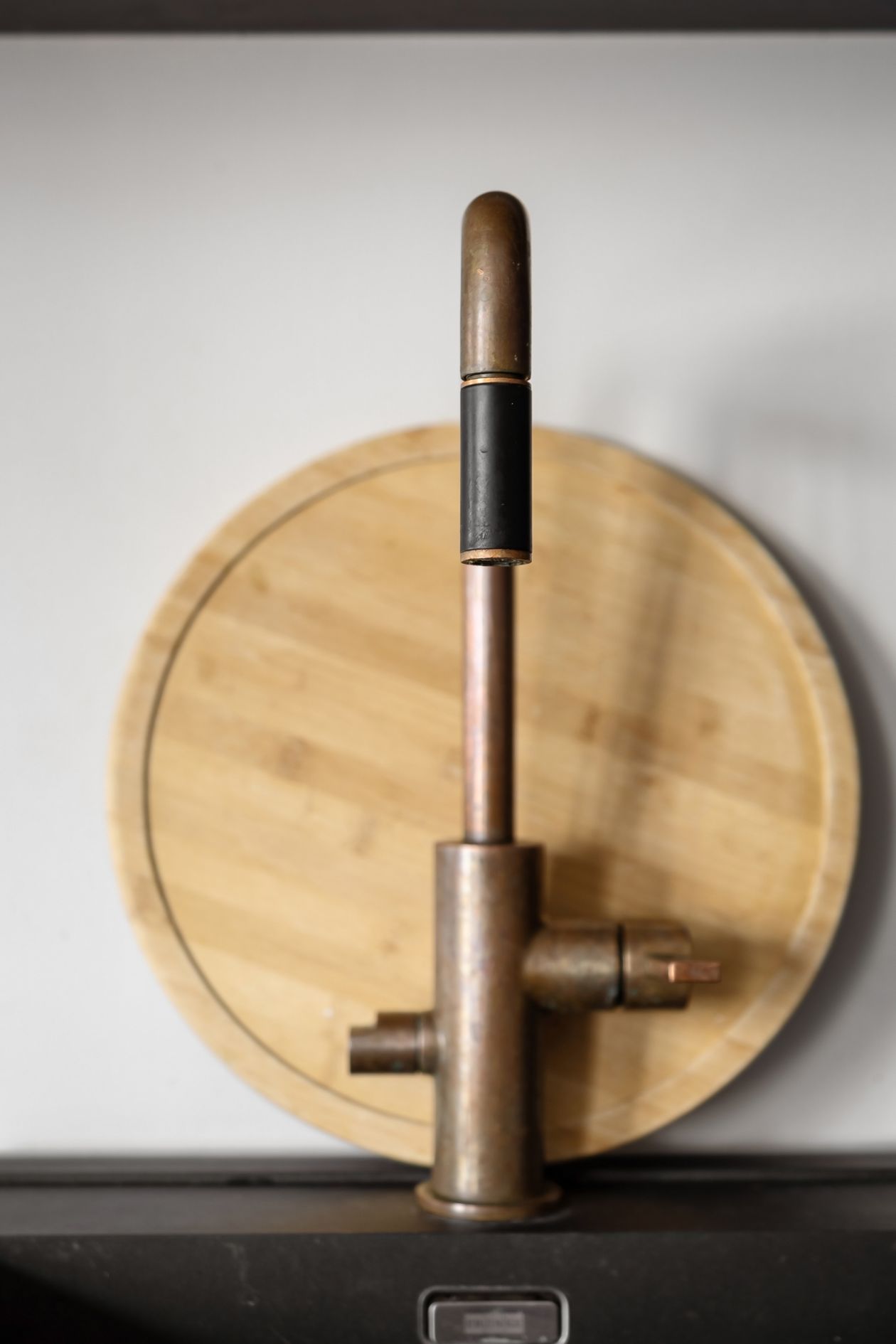 Aged bronze kitchen faucet beside a wooden cutting board