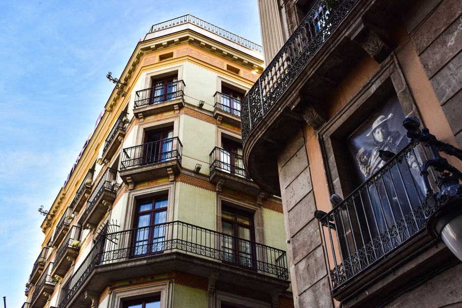 Vista en ángulo bajo de un edificio de apartamentos europeo con balcones ornamentados y un cielo azul de fondo.