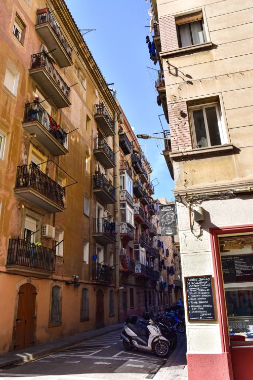 Free Narrow city street with apartment buildings and motor scooters in sunlight. Stock Photo