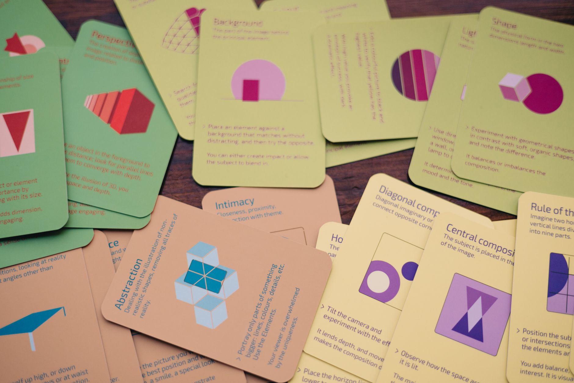 A variety of colorful game cards with geometric shapes scattered across a wooden table.
