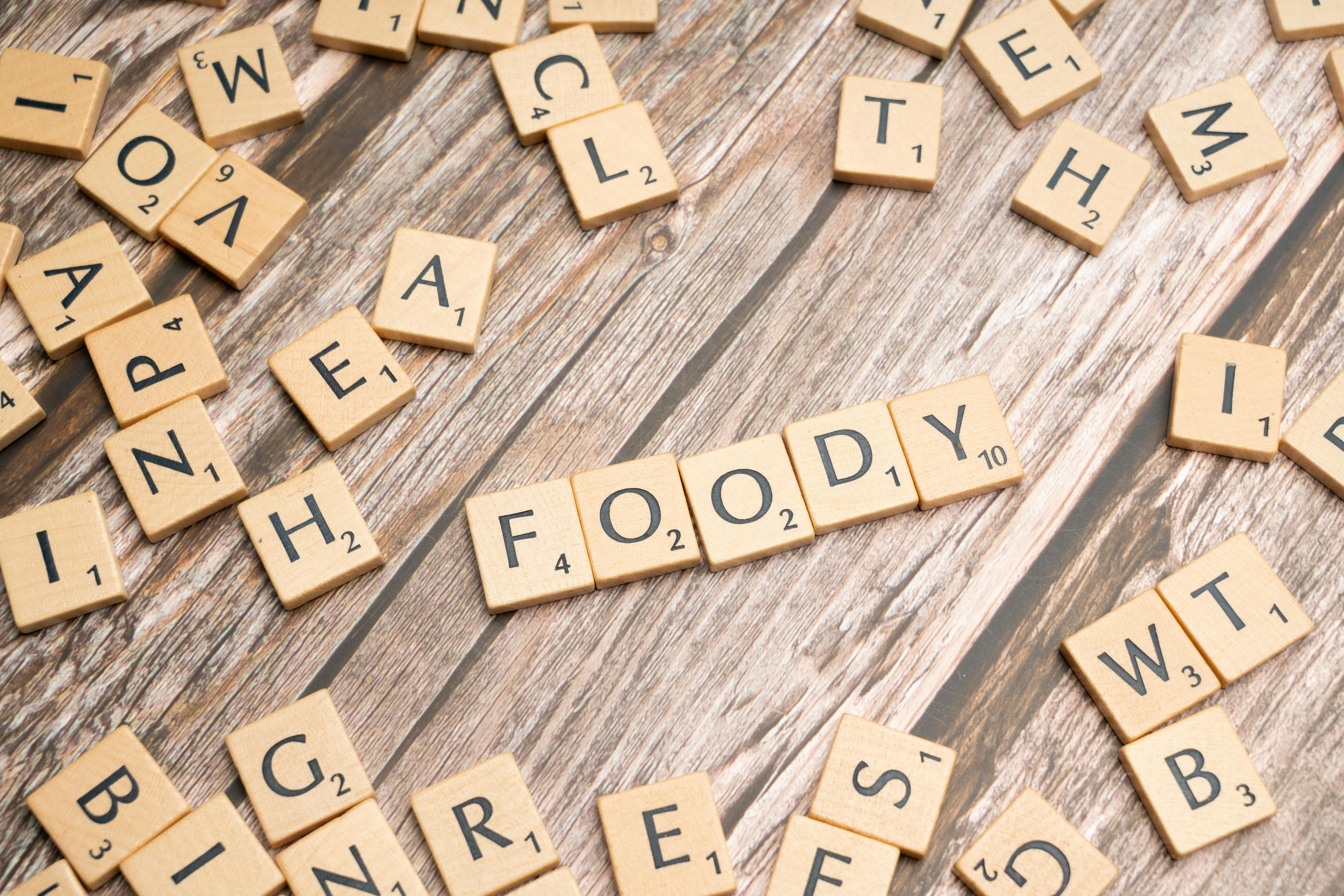 Scrabble-style wooden tiles forming the word 'Foody' on a wooden surface.