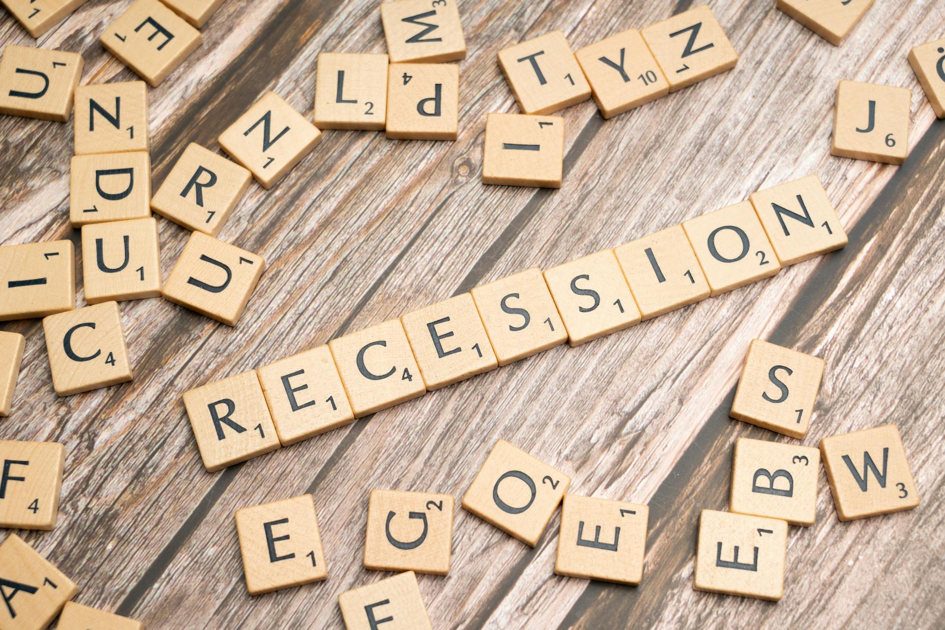 Wooden letter tiles on a wooden surface spell out the word "Recession," symbolizing economic downturn.