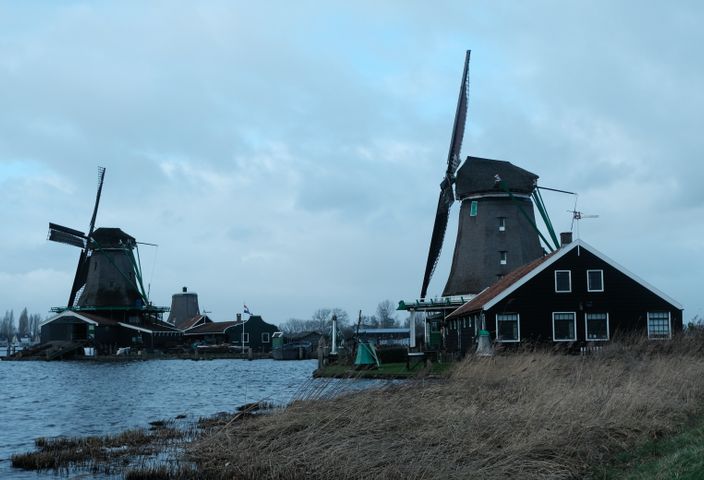 Explore the iconic windmills of Zaanse Schans against a dramatic cloudy sky in this captivating landscape shot.