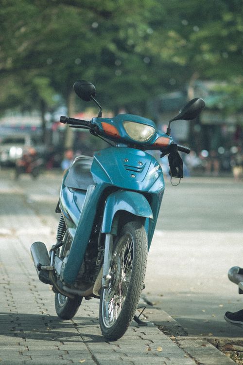 Free A blue motorbike parked on an urban sidewalk, surrounded by a blurred cityscape. Stock Photo