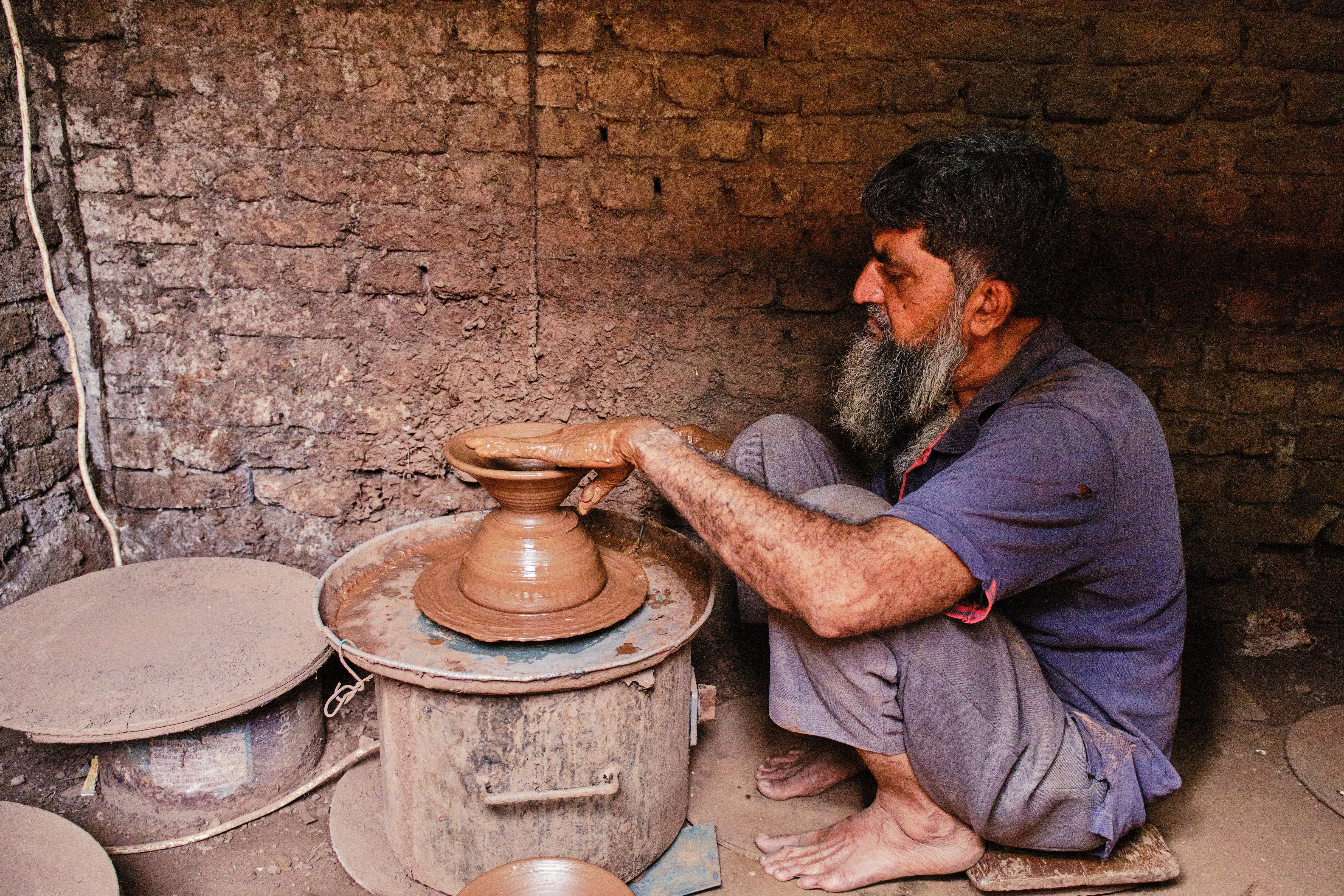 An experienced artisan skillfully shapes clay into a pot on a pottery wheel in a rustic workshop.