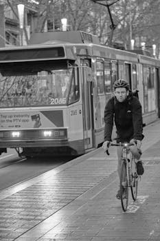 A cyclist rides alongside a tram on a city street captured in black and white.