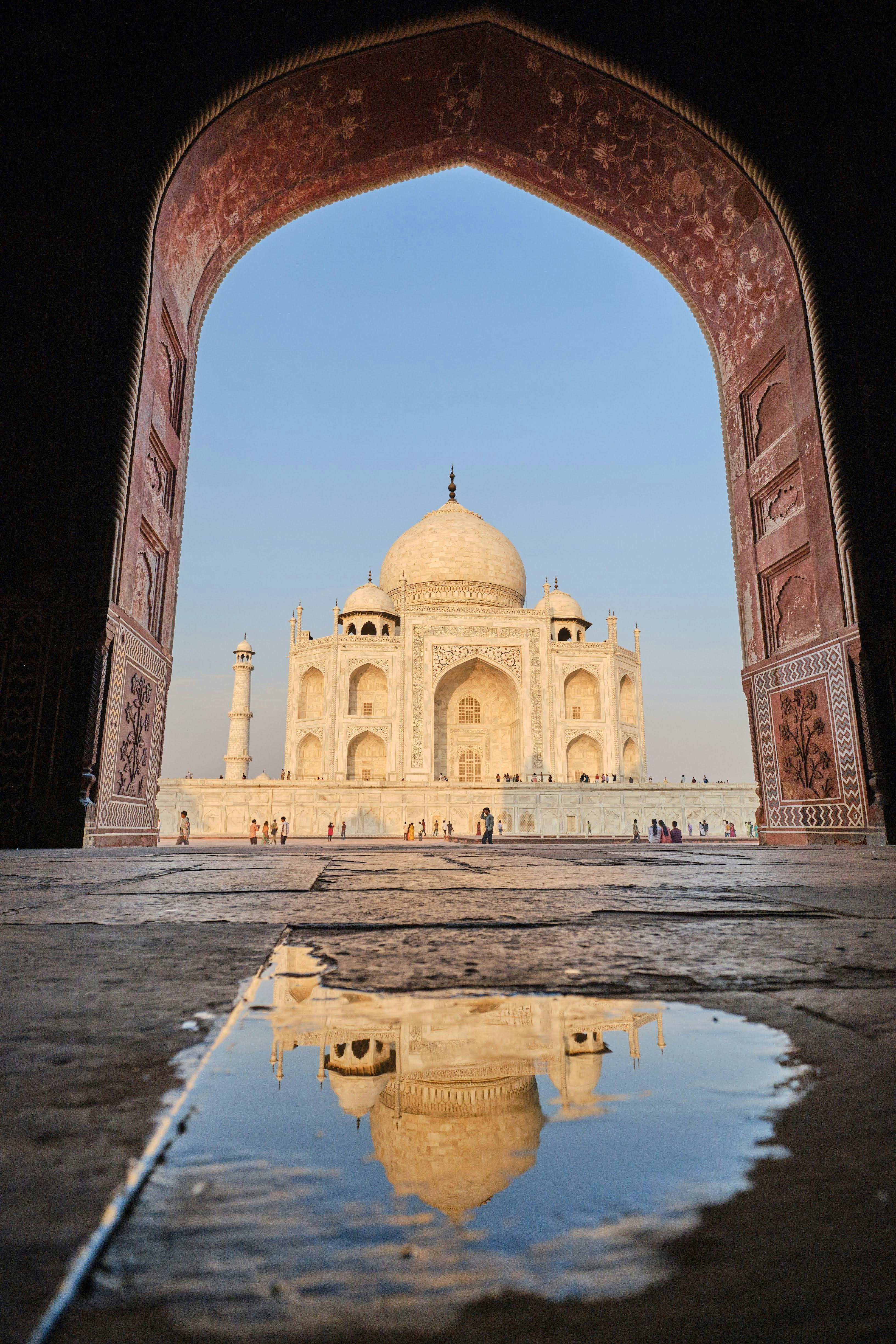 A stunning view of the Taj Mahal framed by an ornate arch with a reflection in a puddle.