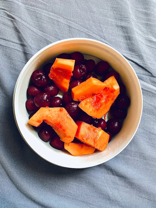 A bowl of fruit and melon on a bed