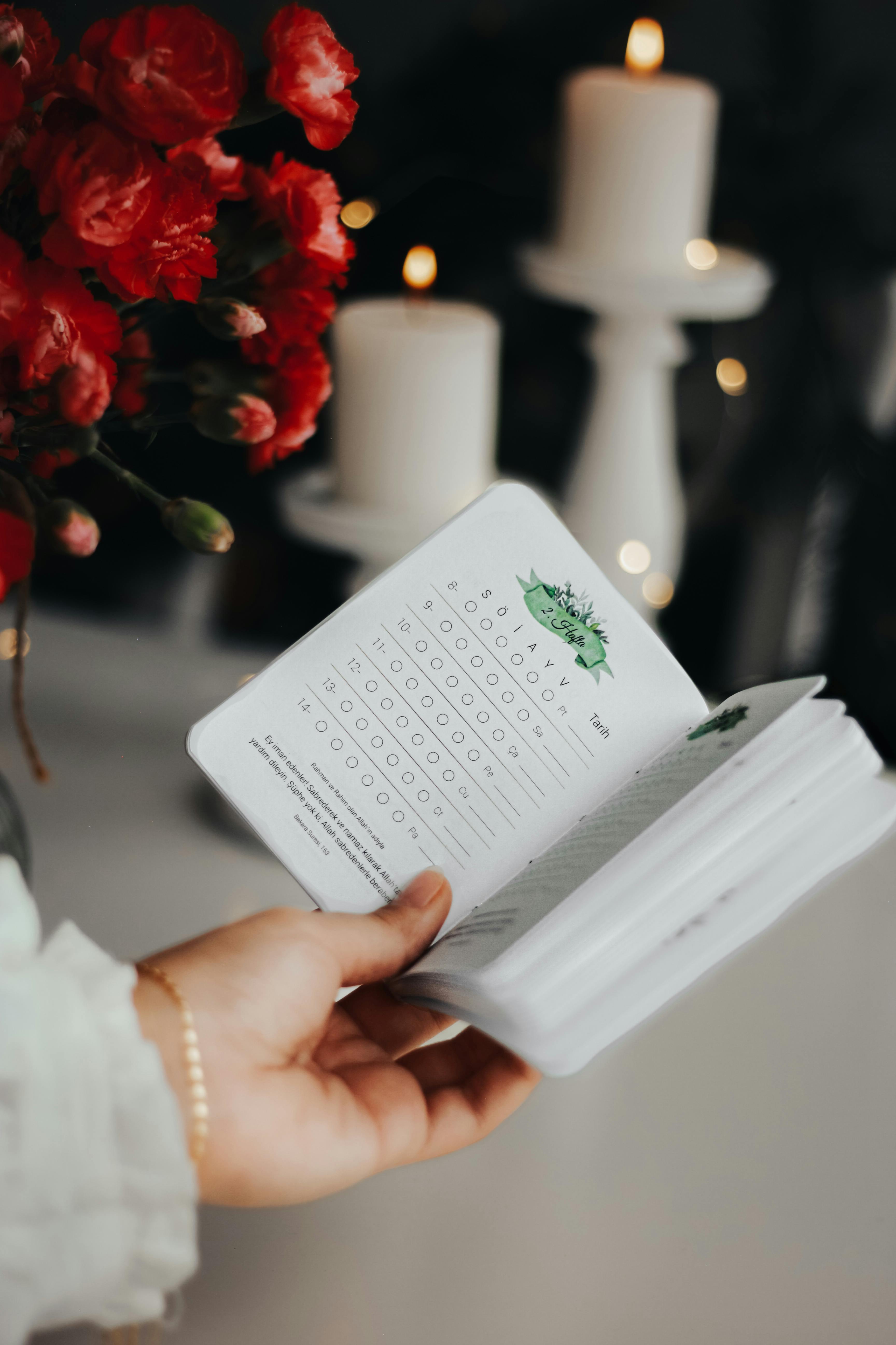 A serene indoor scene featuring an open book, red flowers, and burning candles, creating a cozy ambiance.