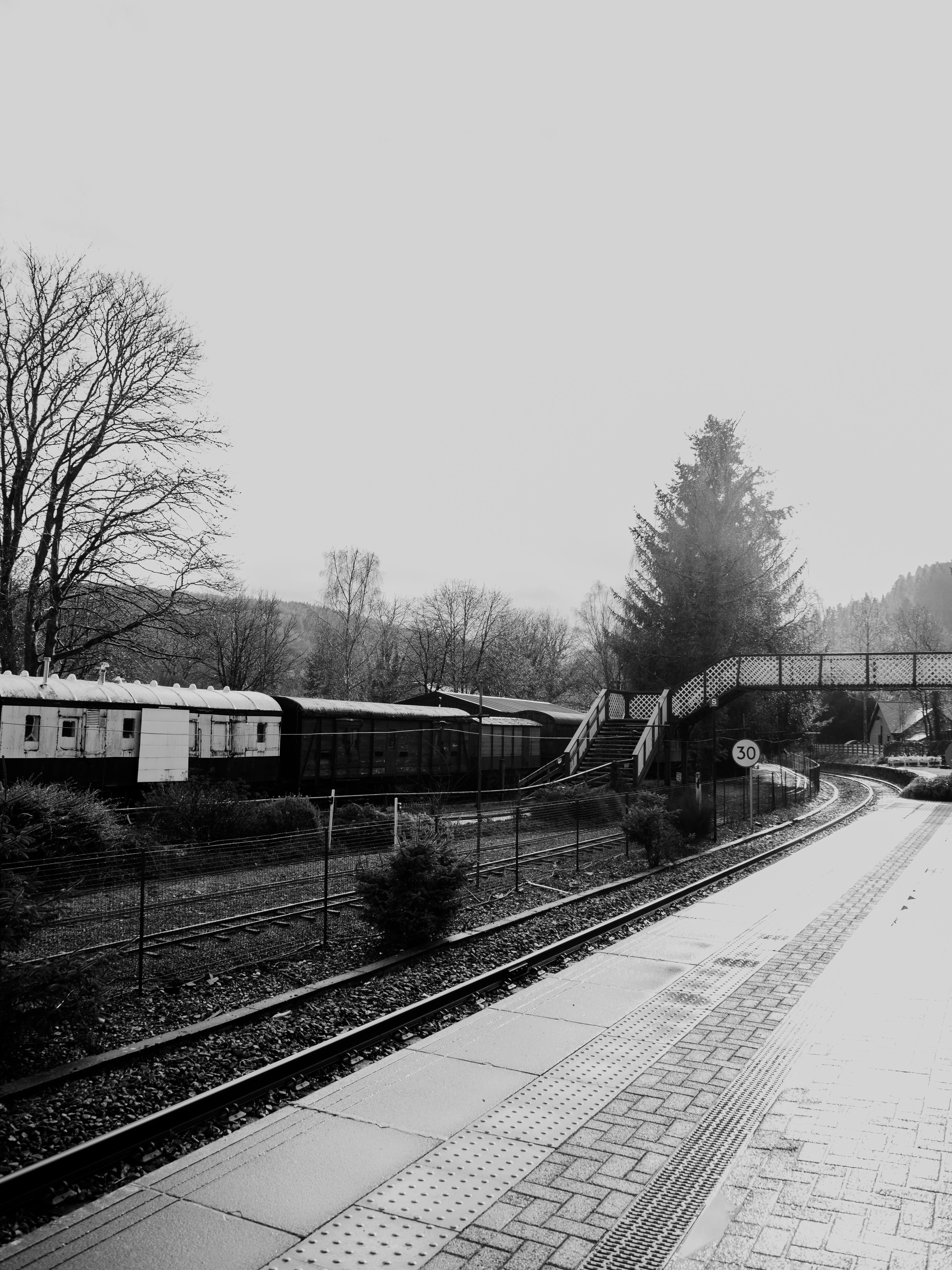 Black and white photo of a railway and footbridge in Betws-y-Coed, Wales, capturing a serene winter morning.