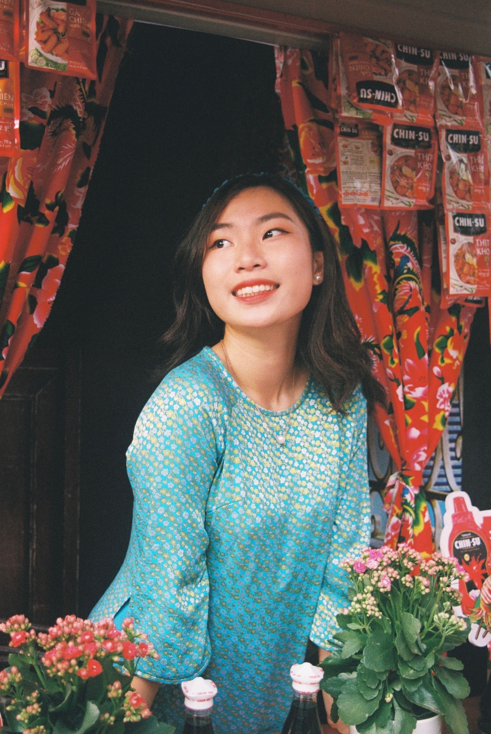 Portrait of a smiling Asian woman in vibrant traditional attire with floral backdrop.