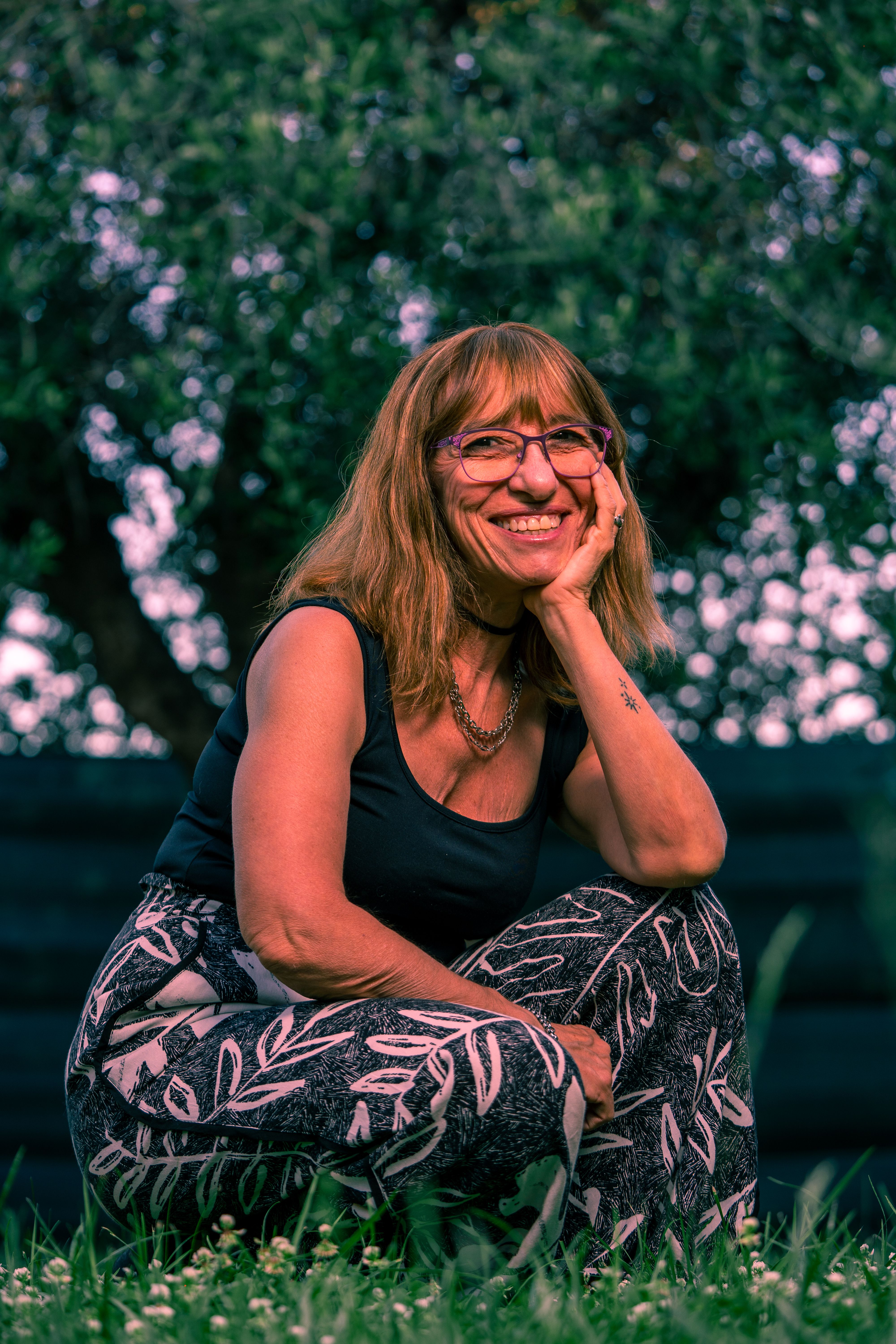 Elderly woman with eyeglasses smiling while sitting outdoors in summer light.