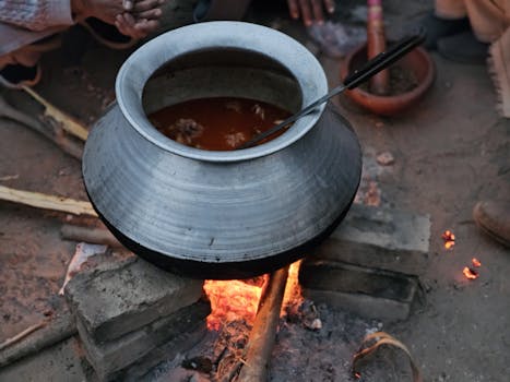Traditional cooking pot with stew simmering over an outdoor bonfire.