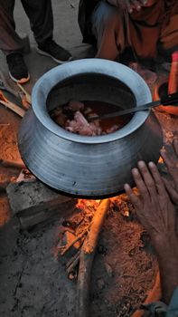 Hands prepare a traditional stew in a pot over an open campfire. Rural cooking scene.
