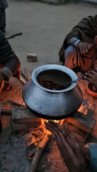 A cozy rural scene depicting people cooking over an open flame with a large pot.
