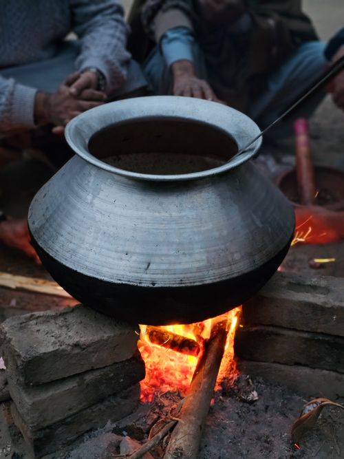 Free A rustic scene of cooking in a silver pot over a bonfire with people gathered around. Stock Photo