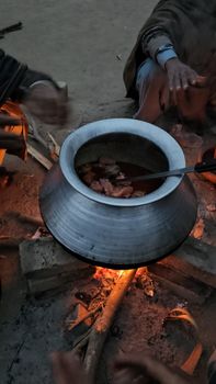 People cooking stew over an open fire in a rural setting.