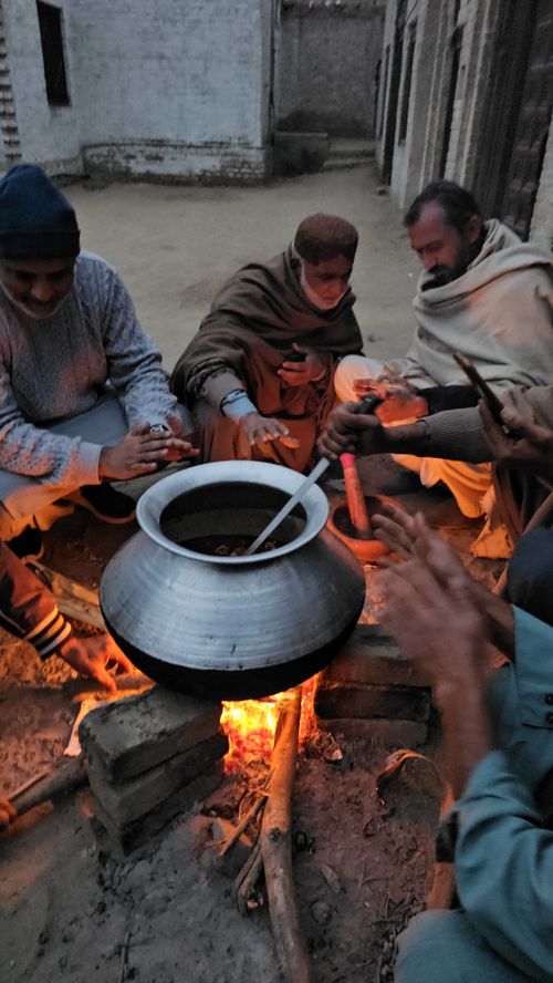 Free Group of men cooking over a bonfire outdoors. Rural setting, traditional pot. Stock Photo