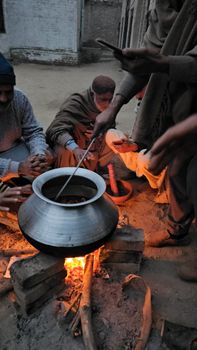 Men cooking over a bonfire in a rural village setting during the evening.