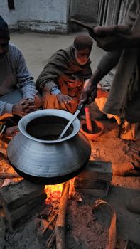 A group of people cooking outdoors over an open fire using a large pot.
