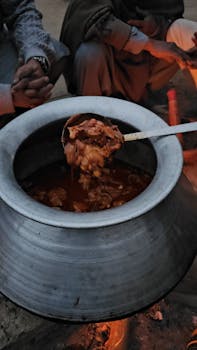 Close-up of a stew being prepared in a large pot over an open flame during an outdoor gathering.