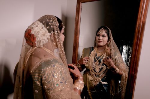 Free A bride in traditional Indian clothing admires herself in the mirror, adorned with gold jewelry and a veil. Stock Photo