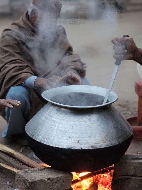 Free A rural setting where people cook over a bonfire using a large silver pot, emitting steam. Stock Photo