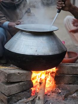 Rural scene of traditional cooking with a large metal pot over an open bonfire.