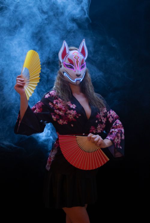 Free A captivating portrait of a woman in a fox mask holding fans, surrounded by smoke and mystery. Stock Photo