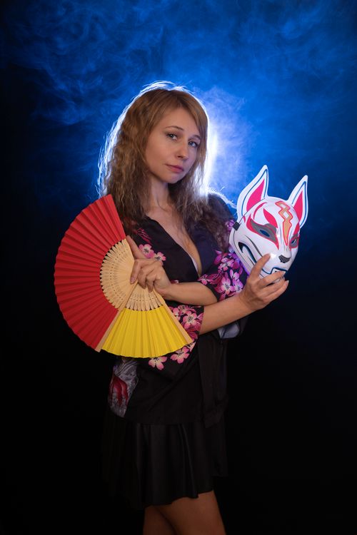Free Caucasian woman posing with a fan and fox mask in studio lighting. Stock Photo