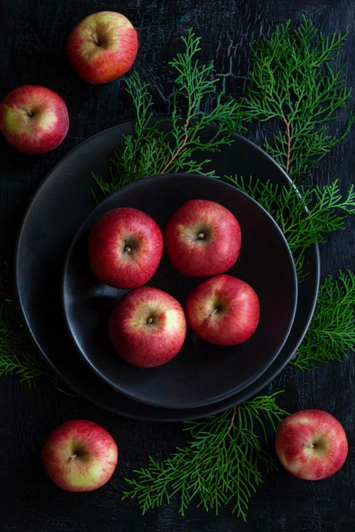 Free A minimalist still life of red apples on black plates with green branches, flat lay style. Stock Photo