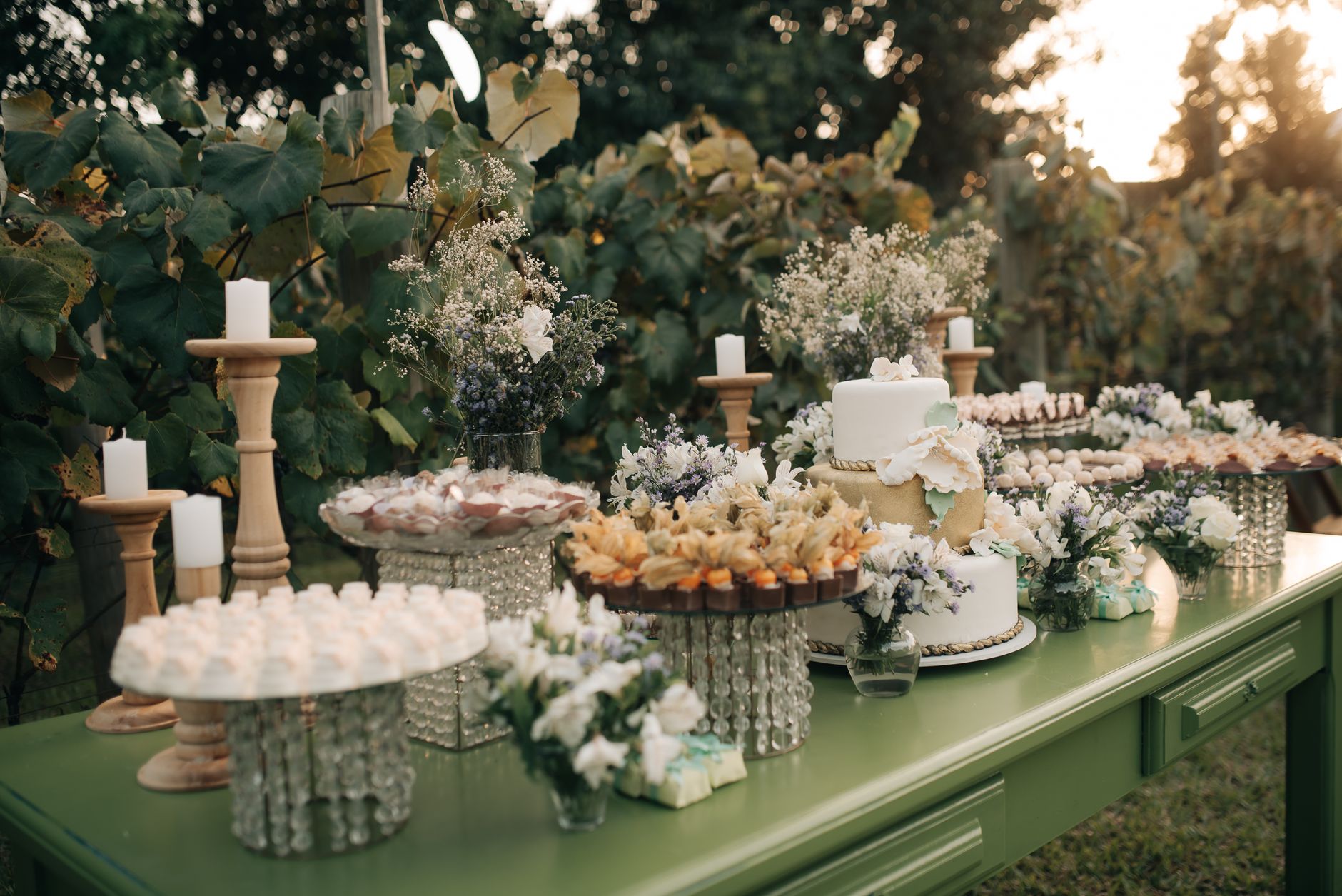 Elegant dessert table setup with cakes and flowers at an outdoor garden wedding reception.