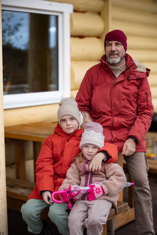 Free A family sitting together in winter clothing outside a wooden cabin. Stock Photo