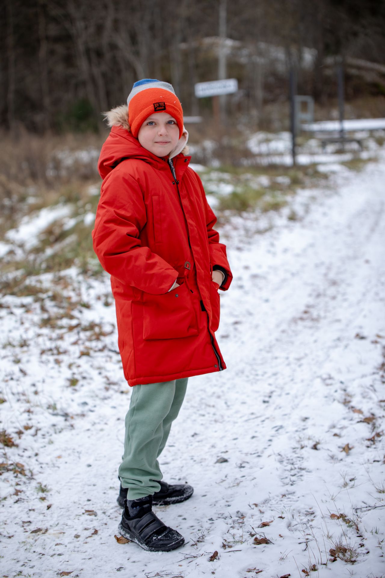Boy in a red winter puffer coat and orange beanie standing on a snowy road