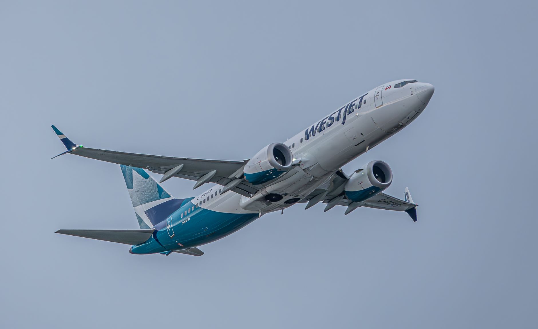 Photo by Airborne YVR A WestJet commercial airplane soaring with engines visible, against a clear blue sky.