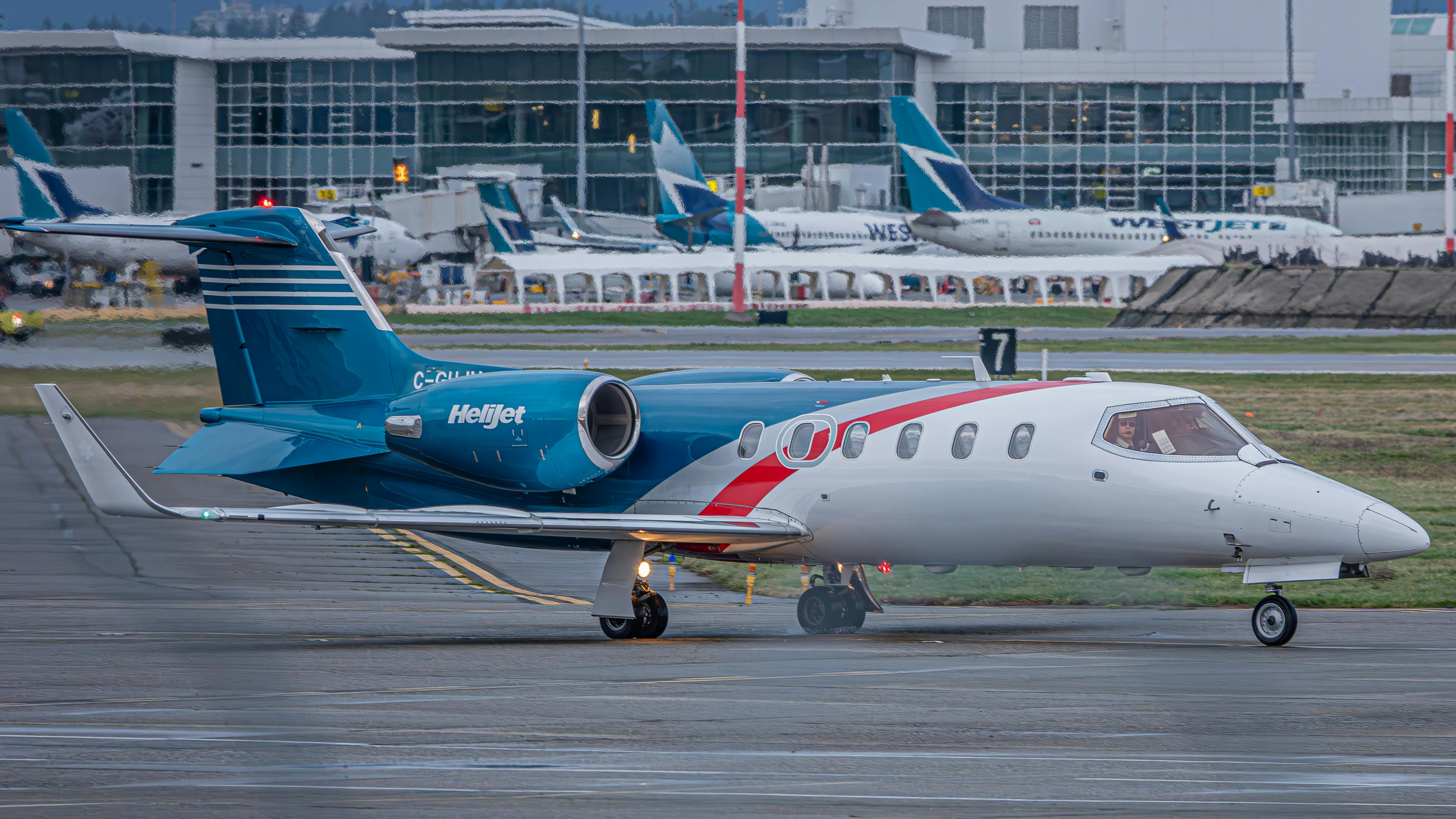A Helijet aircraft positioned on an airport tarmac with terminal in the background.