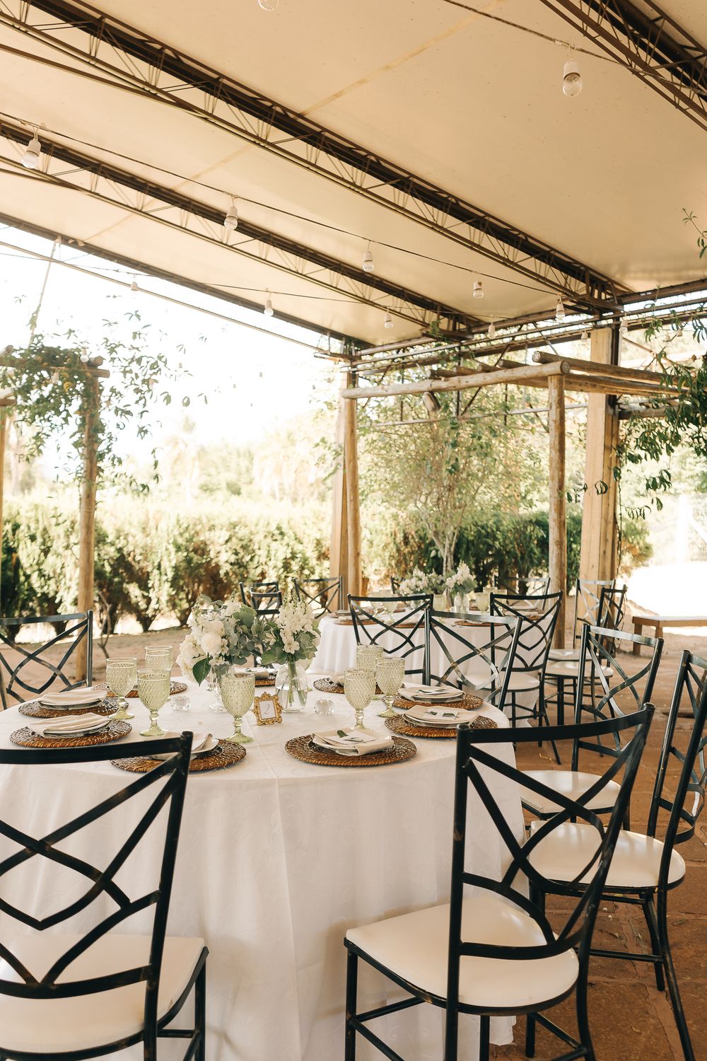 Outdoor wedding gathering with elegant tables and chairs under a canopy