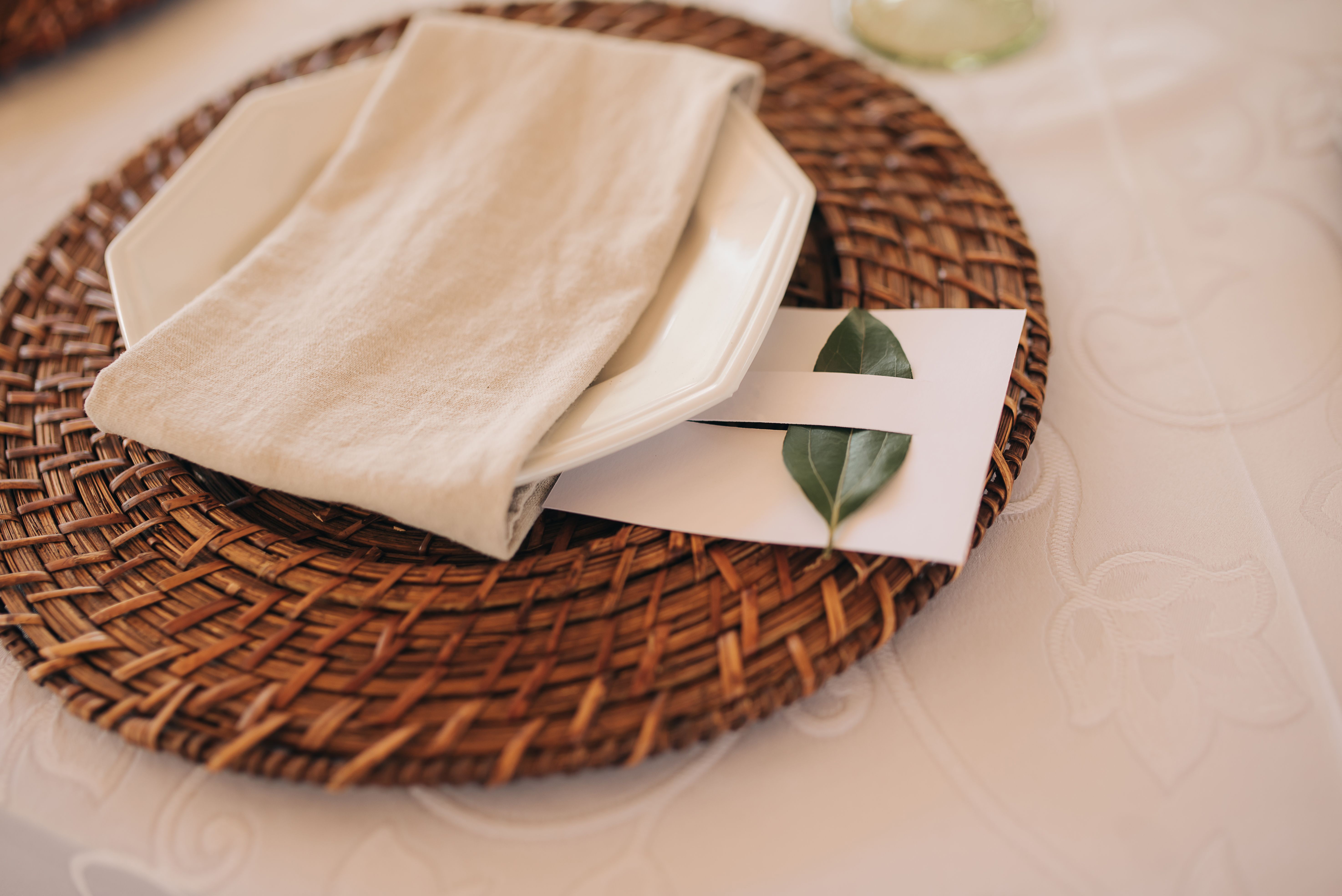 Close-up of a table setting with a woven placemat, ceramic plate, and decorative leaf.