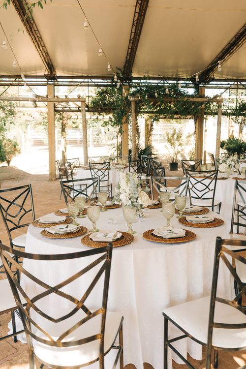 Tables set with place settings and floral centerpieces at an outdoor wedding reception under a canopy