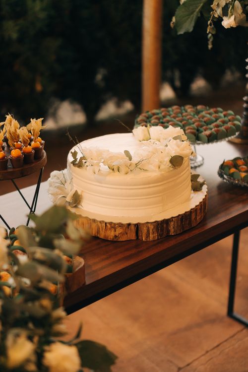 Free A beautifully decorated white cake displayed on a rustic wooden table for an outdoor celebration. Stock Photo