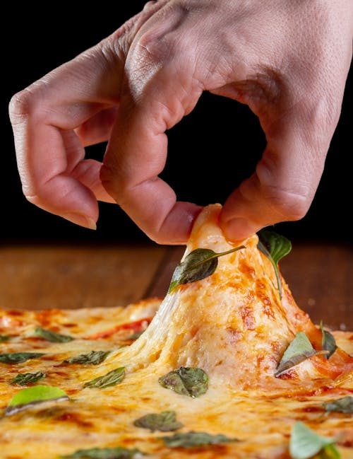 Hand Holding Melted Cheese on a Pizza